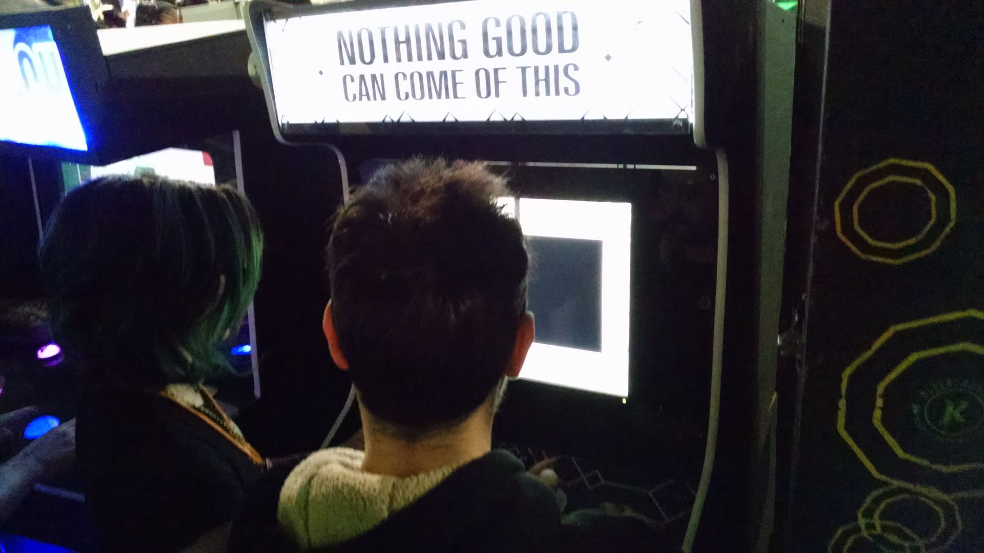 Two people playing on the Nothing Good Can Come Of This arcade machine